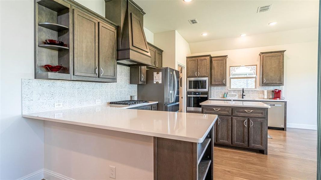 Kitchen featuring wood-finish flooring, white countertops, built-in stainless steel appliances, a center island with additional storage, and a tiled backsplash