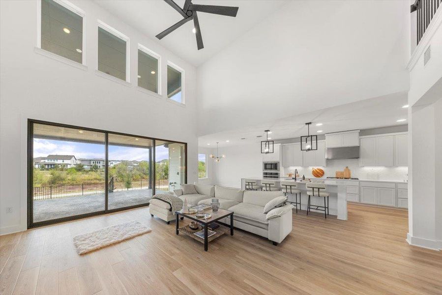 Living room with light wood-style flooring, a high ceiling, a chandelier, recessed lighting, and a ceiling fan Living room with light wood-style flooring, a high ceiling, a chandelier, recessed lighting, and a ceiling fan