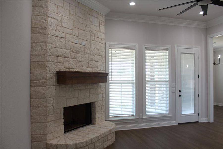 Unfurnished living room with a ceiling fan, a stone fireplace, ornamental molding, wood finished floors, and baseboards Unfurnished living room with a ceiling fan, a stone fireplace, ornamental molding, wood finished floors, and baseboards