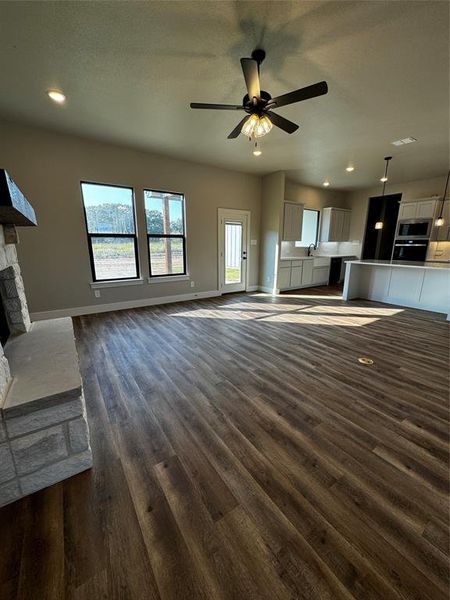 Unfurnished living room with ceiling fan, sink, a stone fireplace, a textured ceiling, and dark hardwood / wood-style flooring