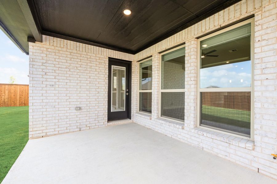 Covered back patio with concrete floor, black door, and large windows on white brick exterior