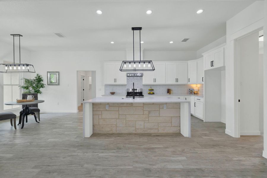 Spacious kitchen featuring an expansive stone-clad island, white shaker cabinetry with dark hardware, a subway tile backsplash, and recessed lighting