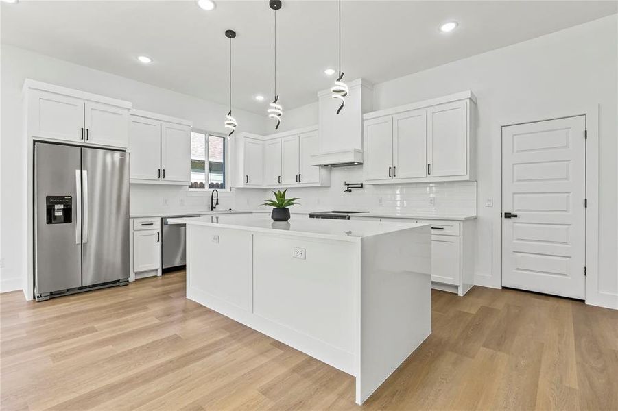 Kitchen with stainless steel appliances, a kitchen island, light countertops, recessed lighting, and white cabinets