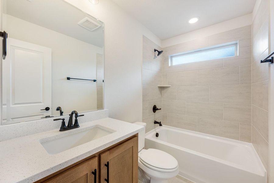 Bathroom with quartz vanity, wood cabinets, tub-shower combo with tile surround, and black fixtures Bathroom with quartz vanity, wood cabinets, tub-shower combo with tile surround, and black fixtures