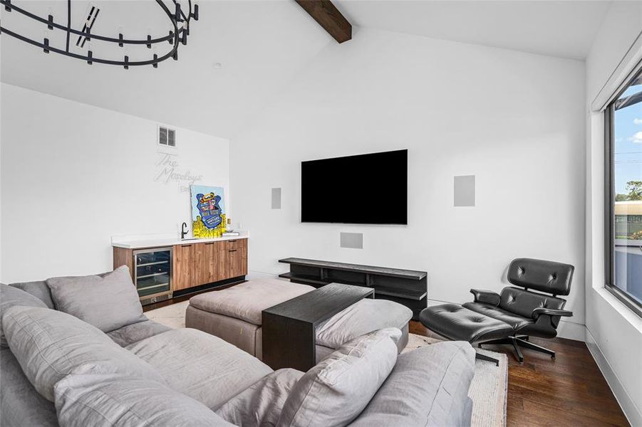 This spacious second-floor game room offers the perfect blend of entertainment and relaxation, with vaulted ceilings and a dramatic chandelier adding to the open, airy atmosphere. A built-in wet bar ensures convenience for hosting gatherings and features custom wood cabinetry, a built-in beverage cooler, and a modern black faucet.