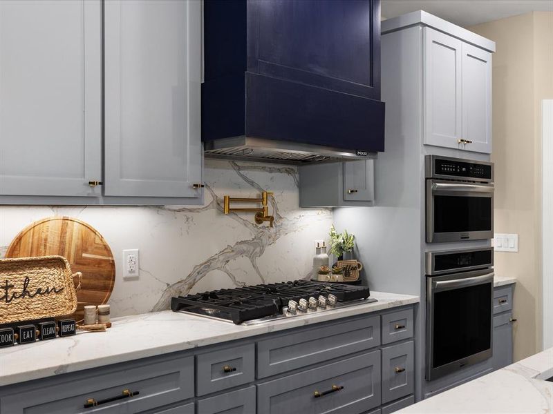 Kitchen featuring light stone counters, stainless steel appliances, and gray cabinetry