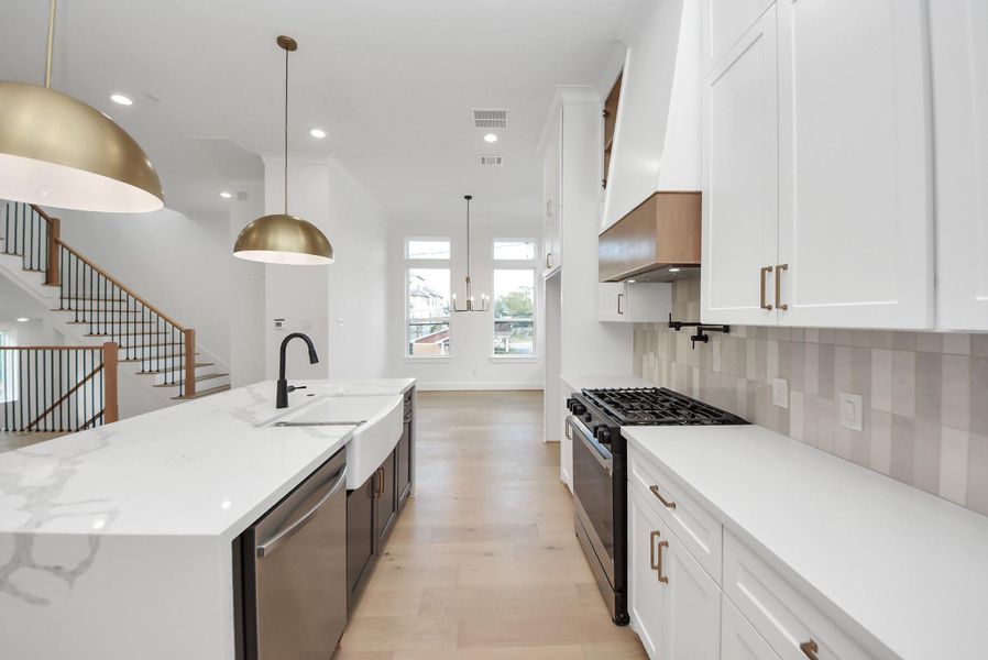 A sleek, entertainer-friendly kitchen with white cabinetry, a spacious marble island, and elegant brass pendant lighting. The built-in gas cooktop, open layout, and natural light make this space ideal for both daily living and hosting.