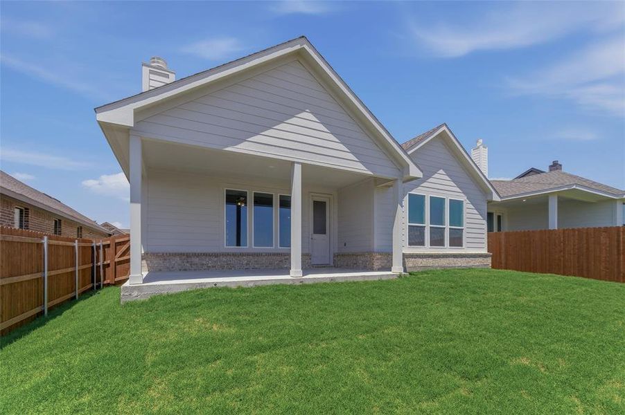 Rear exterior featuring a covered patio, expansive lawn, and white siding with stone accent skirting