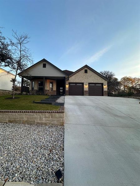 View of front of house with a porch, concrete driveway, brick siding, and an attached garage