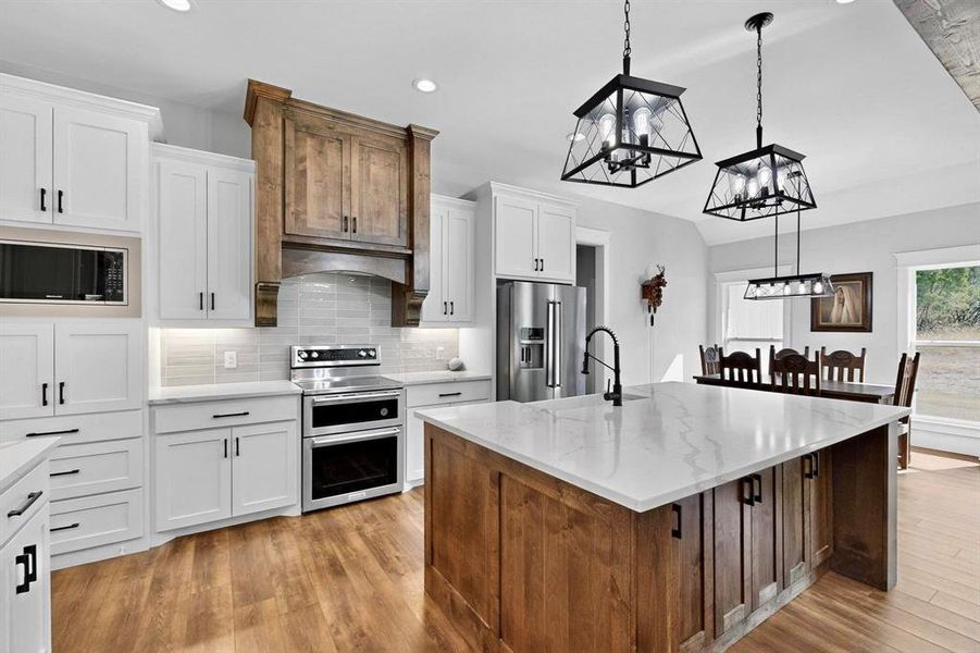 Kitchen with tasteful backsplash, stainless steel appliances, white cabinetry, a kitchen island with sink, and recessed lighting