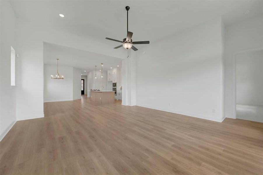 Spacious open-concept interior featuring light wood-finish flooring, recessed lighting, a ceiling fan with integrated light, a gold-tone chandelier, and a kitchen with an island and pendant lighting
