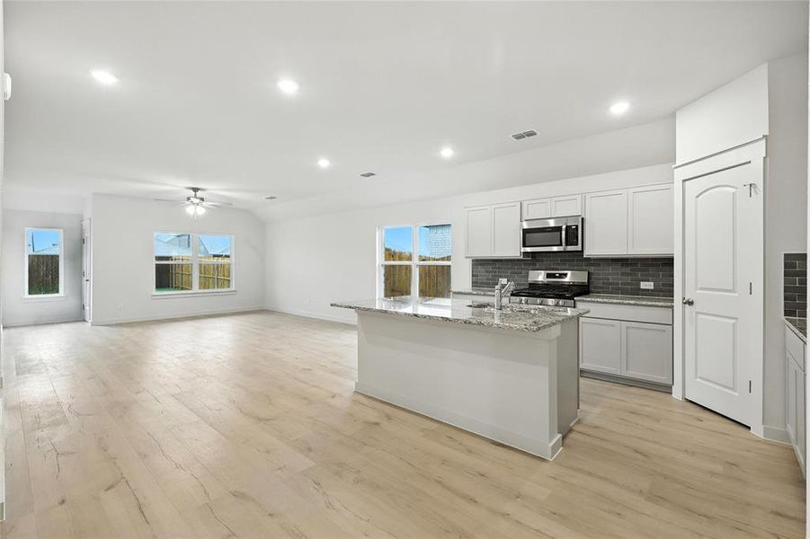 Kitchen with stainless steel appliances, backsplash, light wood-style flooring, ceiling fan, and light stone counters