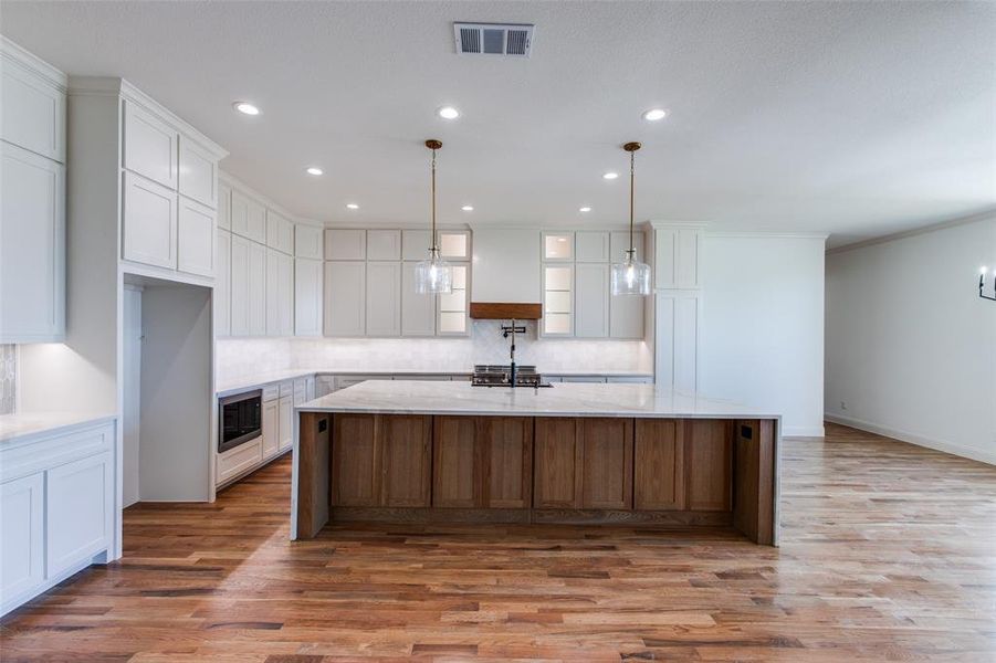 Kitchen with white cabinets, pendant lighting, crown molding, hardwood / wood-style flooring, and a spacious island