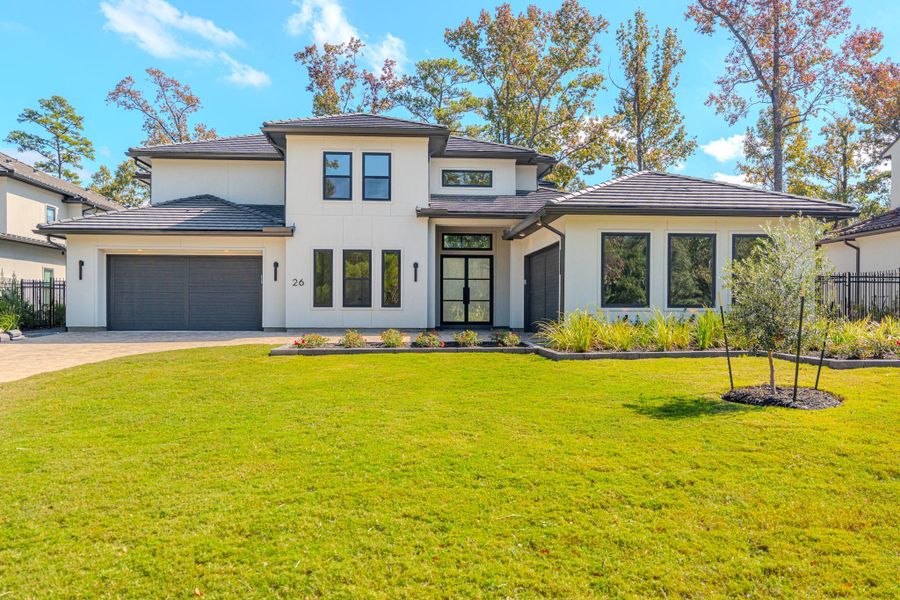 This modern two-story home features a sleek design with large windows, a spacious three-car garage, and well-maintained landscaping. It offers a bright, inviting entrance and is surrounded by mature trees, providing a serene setting.