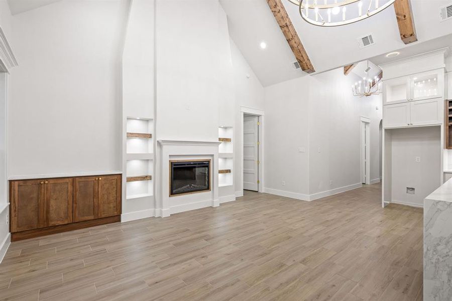 Vaulted living area featuring a fireplace with built-in shelving, wood-finish flooring, exposed ceiling beams, and a chandelier Vaulted living area featuring a fireplace with built-in shelving, wood-finish flooring, exposed ceiling beams, and a chandelier