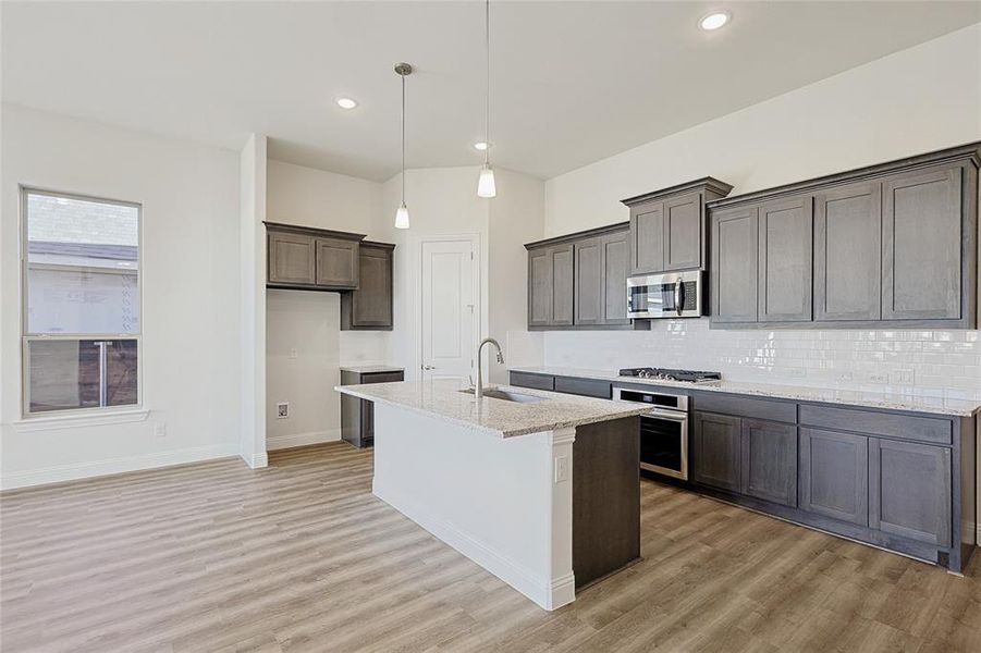 Kitchen featuring light stone countertops, sink, pendant lighting, a center island with sink, and appliances with stainless steel finishes