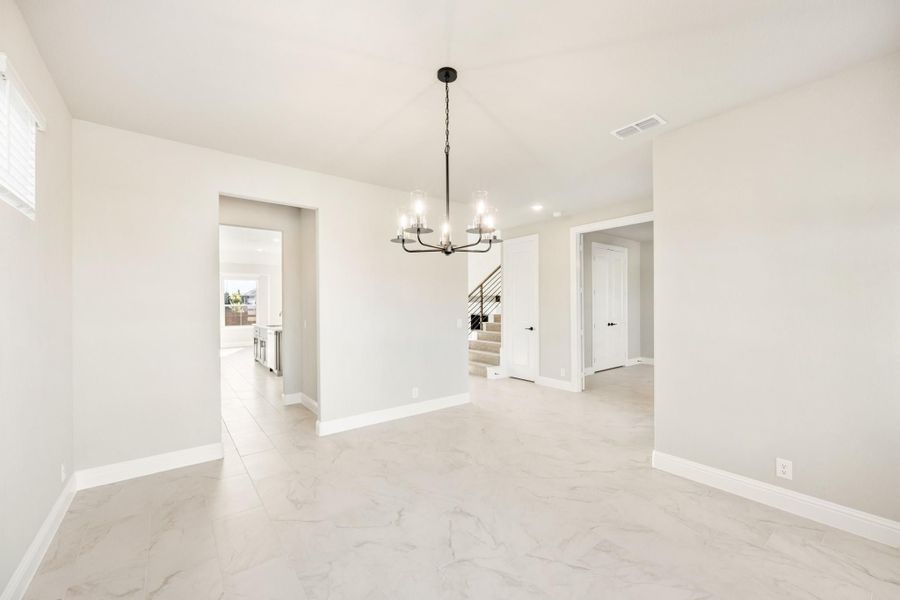 Empty dining room with black chandelier, marble tile floors, and open view to staircase and kitchen