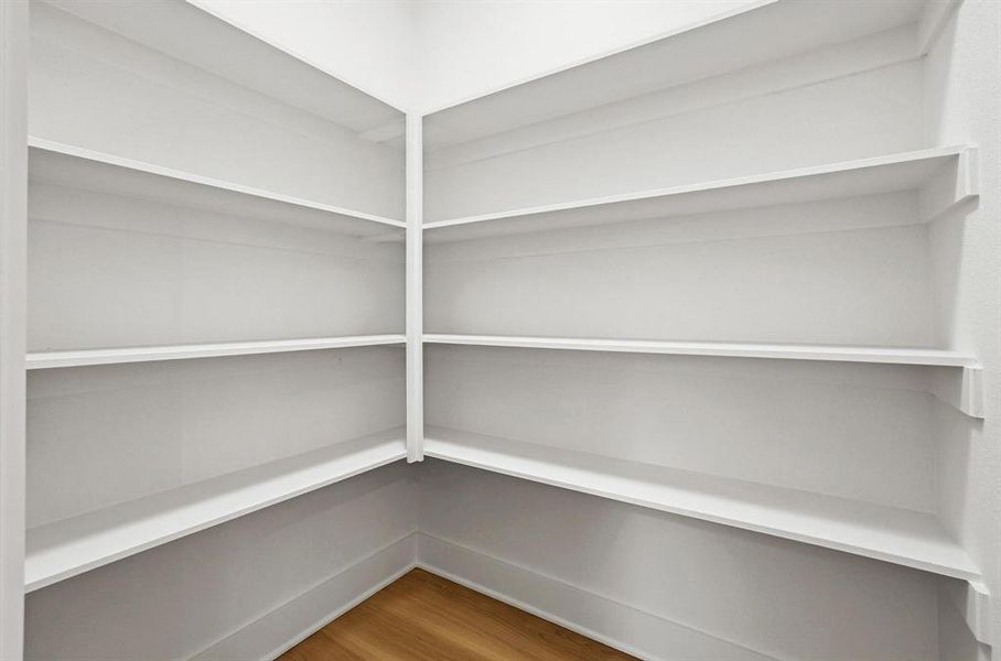 Corner pantry featuring built-in shelving, white finishes, and wood-finish flooring Corner pantry featuring built-in shelving, white finishes, and wood-finish flooring