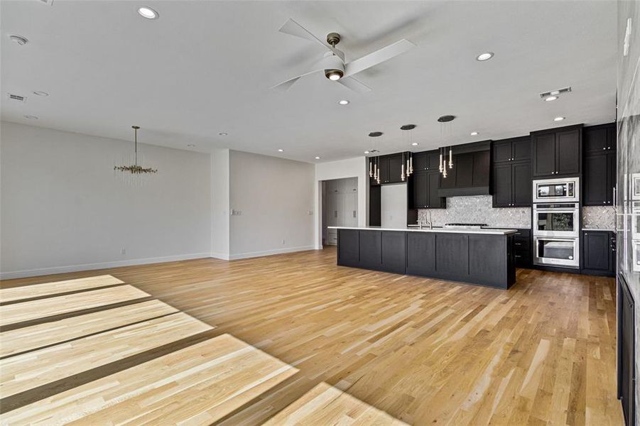 Kitchen with a kitchen island with sink, hanging light fixtures, light wood-type flooring, and tasteful backsplash