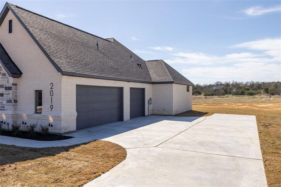 View of side of home with a garage, brick siding, roof with shingles, and concrete driveway