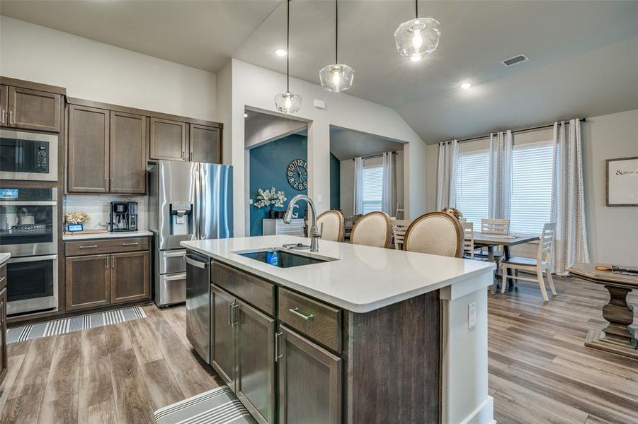 Kitchen with appliances with stainless steel finishes, pendant lighting, light hardwood / wood-style flooring, a center island with sink, and sink