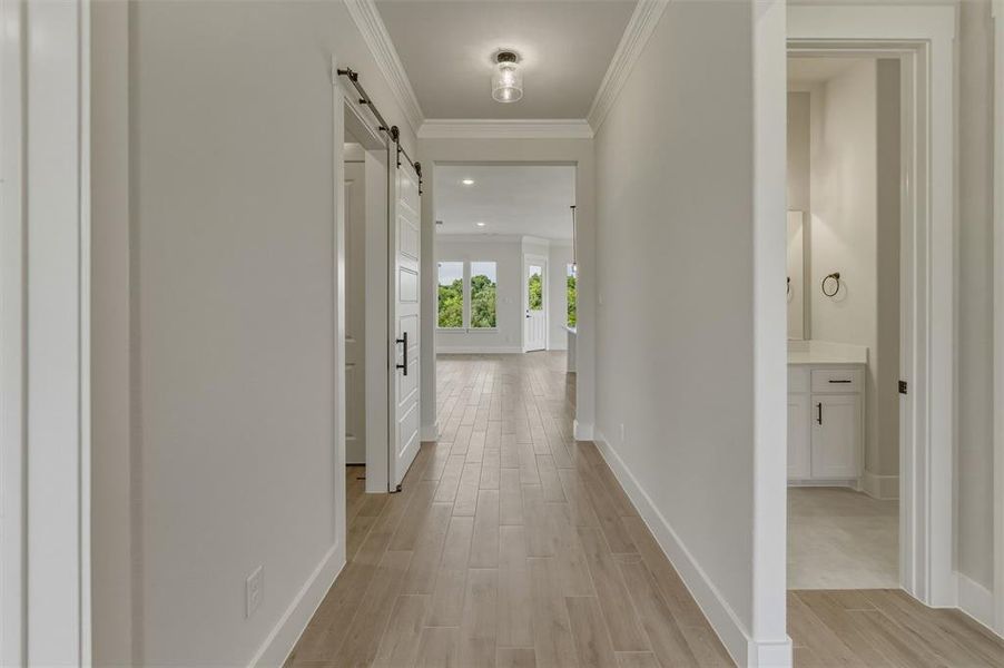 Spacious hallway with light wood-finish flooring, white baseboards, and crown molding Spacious hallway with light wood-finish flooring, white baseboards, and crown molding