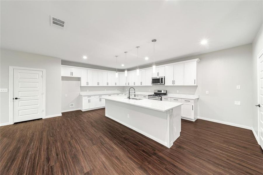 Kitchen featuring white cabinets, stainless steel appliances, a center island with sink, and dark wood finished floors