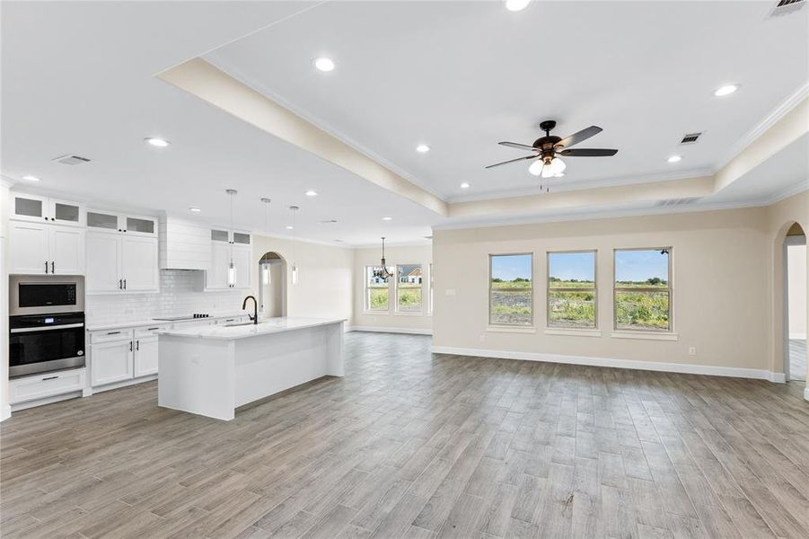 Kitchen featuring an island with sink, hanging light fixtures, decorative backsplash, and a tray ceiling