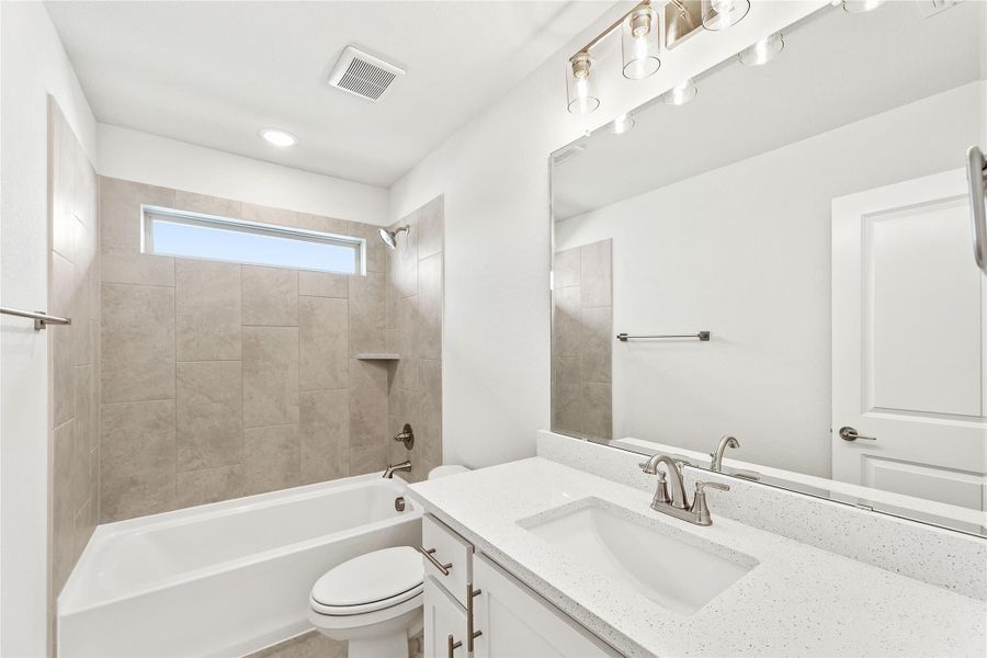 Bathroom with white vanity, quartz countertop, tiled tub-shower combo, and large mirror with overhead lighting Bathroom with white vanity, quartz countertop, tiled tub-shower combo, and large mirror with overhead lighting