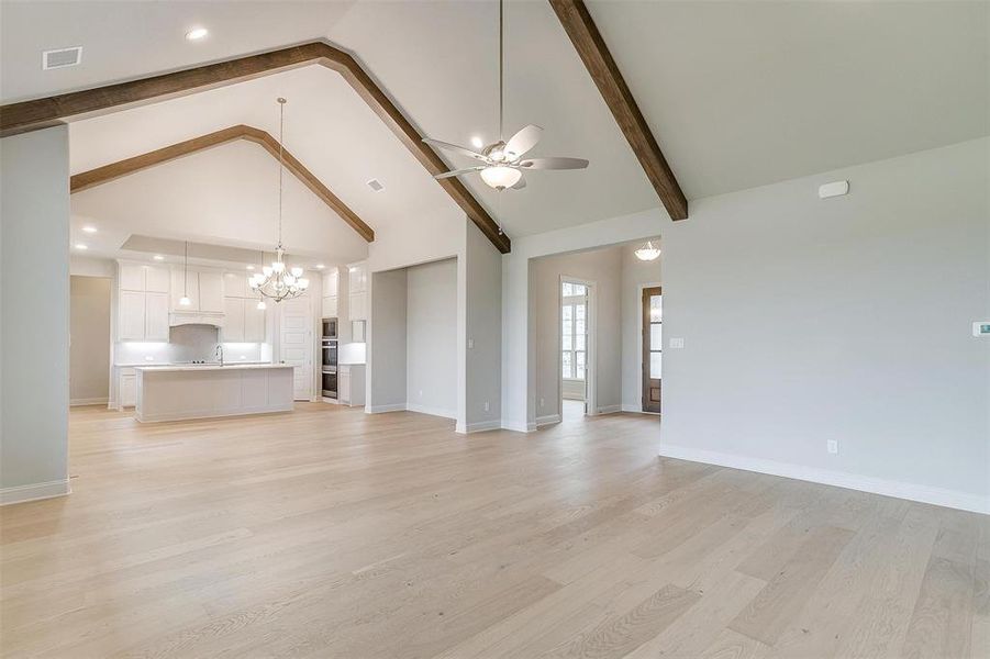 Unfurnished living room featuring beam ceiling, ceiling fan with notable chandelier, light wood-type flooring, and high vaulted ceiling