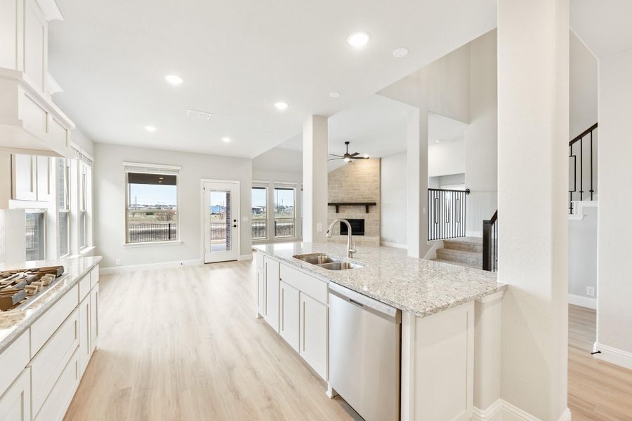 Open-concept kitchen with white cabinets, granite island, and living room with fireplace visible beyond. Open-concept kitchen with white cabinets, granite island, and living room with fireplace visible beyond.