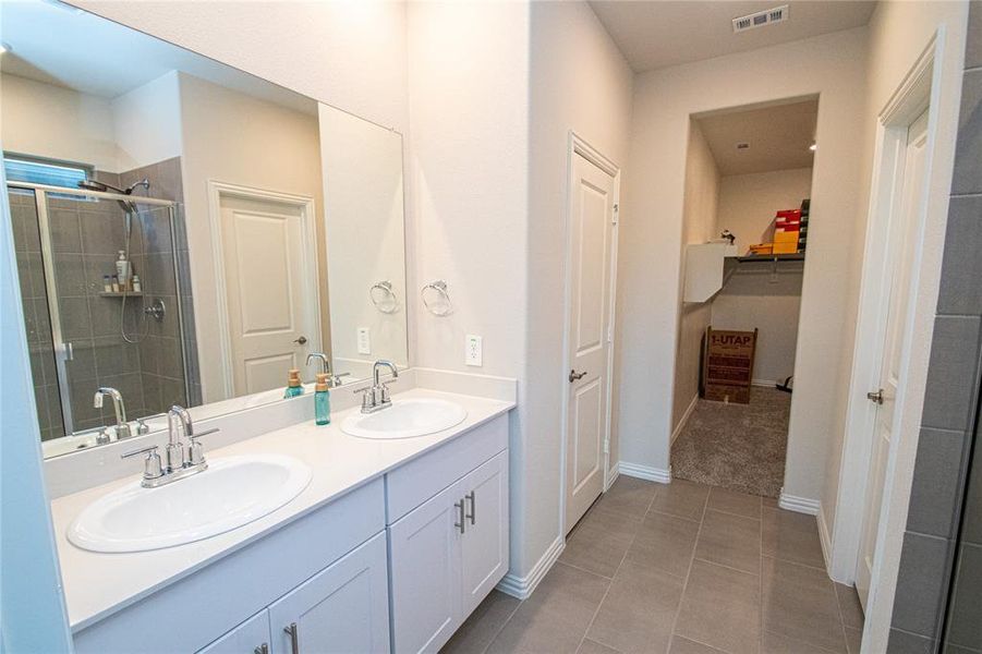 Bathroom with a shower stall, double vanity, a spacious closet, and light tile patterned floors Bathroom with a shower stall, double vanity, a spacious closet, and light tile patterned floors