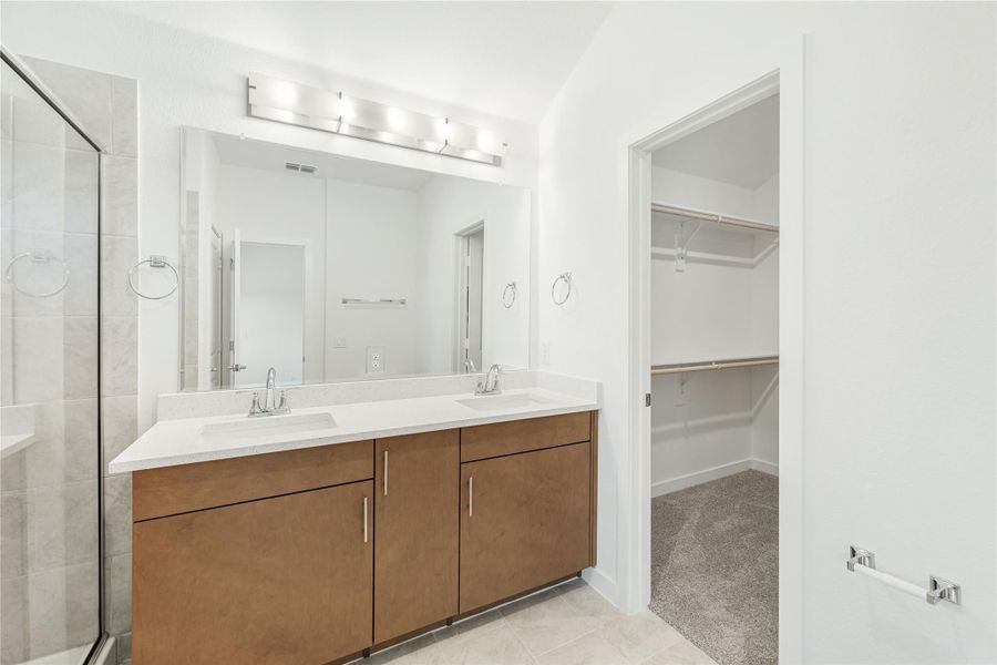 Bathroom with double sink vanity, wood cabinets, glass shower, and walk-in closet entrance