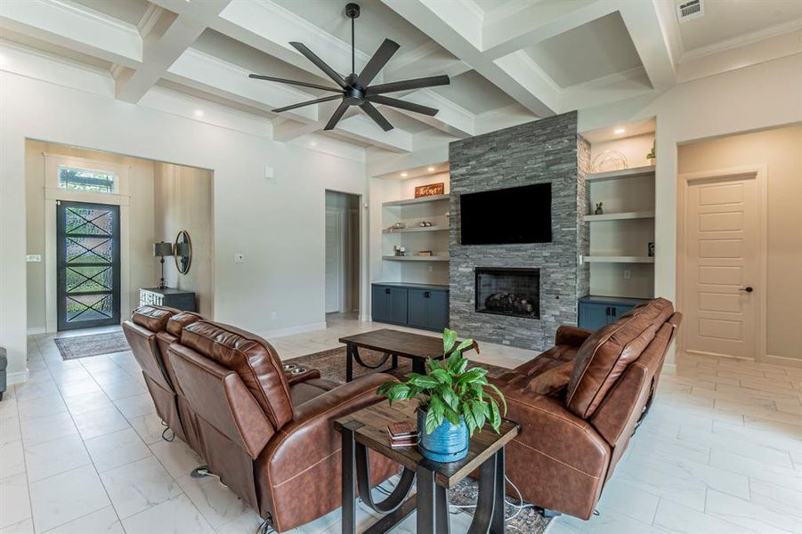 Living area featuring a stone fireplace, ceiling fan, coffered ceiling, built in shelves, and crown molding Living area featuring a stone fireplace, ceiling fan, coffered ceiling, built in shelves, and crown molding