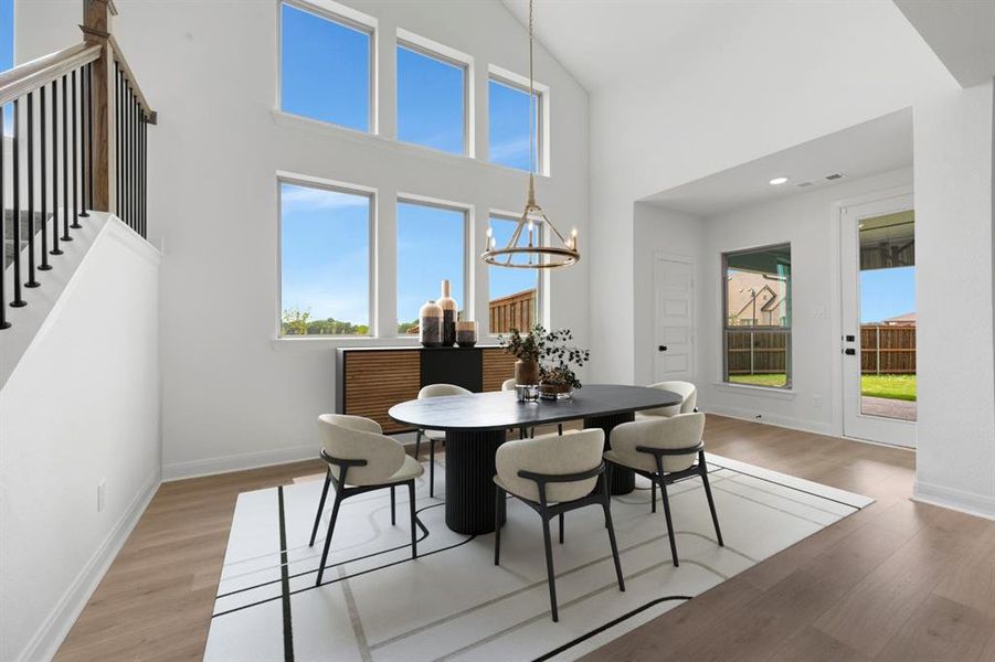 Two-story ceiling with a contemporary chandelier, multiple large windows, wood-finish flooring, white painted walls, and a staircase with a black metal baluster