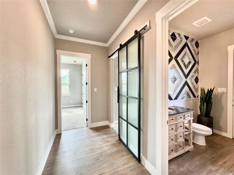 Hallway featuring wood finished floors, crown molding, baseboards, and a barn door