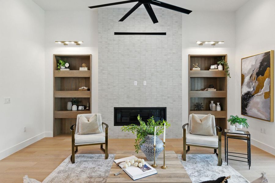 Living area with built in shelves, a fireplace, light wood-style flooring, and ceiling fan Living area with built in shelves, a fireplace, light wood-style flooring, and ceiling fan