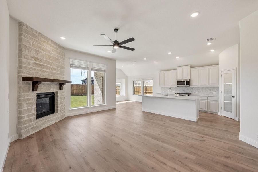 Open living area with stone fireplace, hardwood floors, and kitchen with white cabinets and center island Open living area with stone fireplace, hardwood floors, and kitchen with white cabinets and center island
