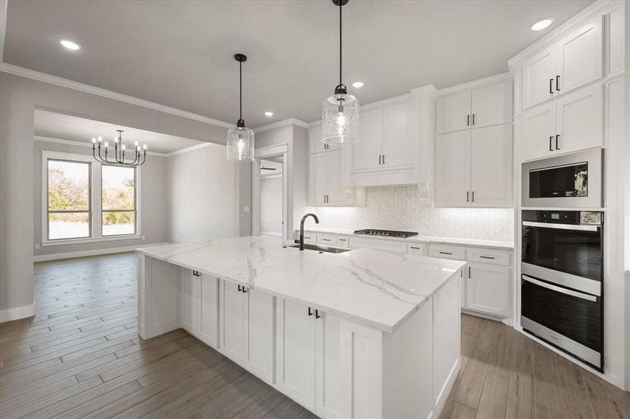 Kitchen featuring a center island with sink, sink, white cabinetry, light stone counters, and light hardwood / wood-style floors