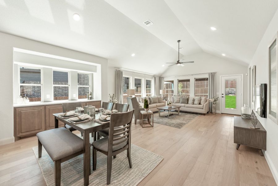 Open-concept dining and living area with vaulted ceiling, hardwood floors, and French doors to backyard