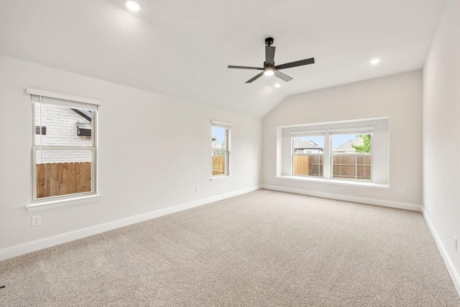 Empty bedroom with vaulted ceiling, ceiling fan, carpet flooring, and three windows Empty bedroom with vaulted ceiling, ceiling fan, carpet flooring, and three windows