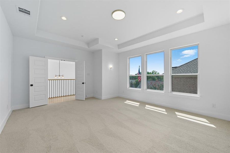 Spare room with a raised ceiling, light colored carpet, recessed lighting, and a chandelier