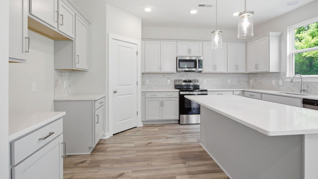 Kitchen with light cabinetry, quartz countertops, tile backsplash, pantry, and window Kitchen with light cabinetry, quartz countertops, tile backsplash, pantry, and window