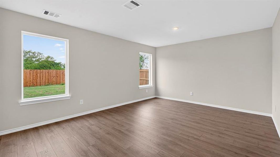 Spacious room featuring wood-finish flooring, light grey walls, white baseboards, and two windows