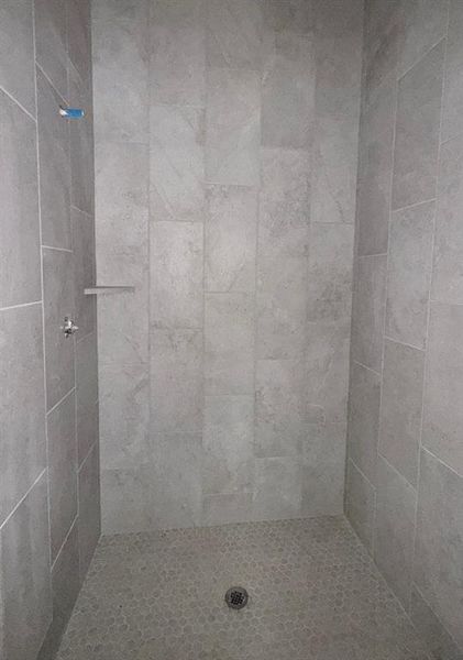 Shower stall featuring large format gray wall tiling and a pebble-finish floor Shower stall featuring large format gray wall tiling and a pebble-finish floor