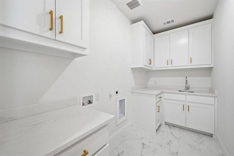 Laundry room featuring white cabinetry with gold-tone hardware, white marble-look countertops, and a stainless steel sink with a high-arc faucet