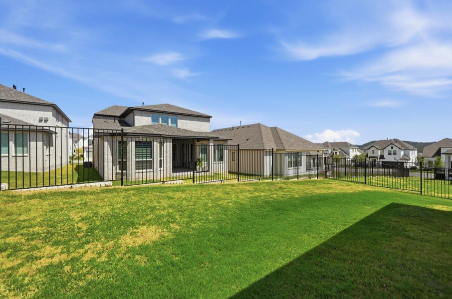 An expansive green lawn sits enclosed by modern black metal fencing under a bright blue sky.