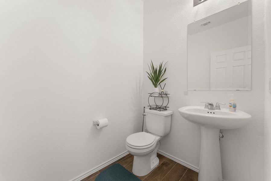 Bathroom featuring toilet, wood finish floors, a sink, visible vents, and baseboards