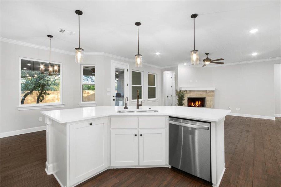 Kitchen featuring dishwasher, a sink, ceiling fan, light countertops, and a warm lit fireplace Kitchen featuring dishwasher, a sink, ceiling fan, light countertops, and a warm lit fireplace