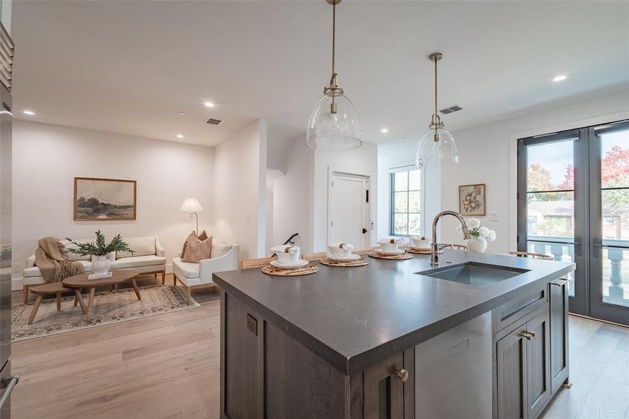 Kitchen with sink, light hardwood / wood-style floors, decorative light fixtures, dark brown cabinets, and a center island with sink